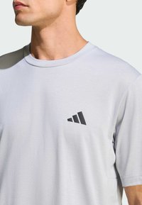 Camiseta de manga corta de color gris claro, hecha de tela suave, con un pequeño logo triangular negro en el área del pecho izquierdo.
