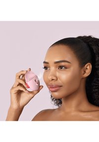 Dispositif portable rose avec une forme arrondie, présentant un design Hello Kitty, un bouton brillant et une surface lisse. Le modèle l'utilise près de son visage.