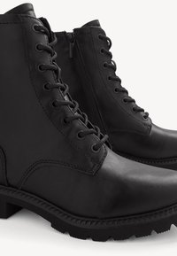 Bottes basses en cuir noir avec lacets à l'avant, fermetures éclair latérales et petits talons carrés sur fond blanc.