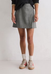 Szara spódnica w kratę z dopasowaną talią i rozszerzanym dołem. Połączona z beżowymi sneakerami i białymi skarpetkami ribbed na codzienny look.