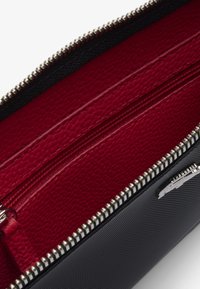 Pochette zippée avec un extérieur texturé noir et un intérieur rouge, accentuée par une fermeture éclair argentée et un design à double compartiment.