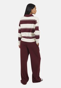 Gestreepte pullover trui in crème en bordeaux, met lange mouwen en een kraag. Wijde bordeaux broek van zachte stof.