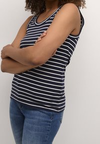 Marinblå rippad linne med vita ränder, rundad halsringning och ärmlös design. Bärs med blå jeans.