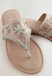 Sandali scivolosi in satin rosa con ricami argentati, dettagli in perline e suola piatta con design a distanziatore per le dita. Texture morbida e motivi dettagliati.