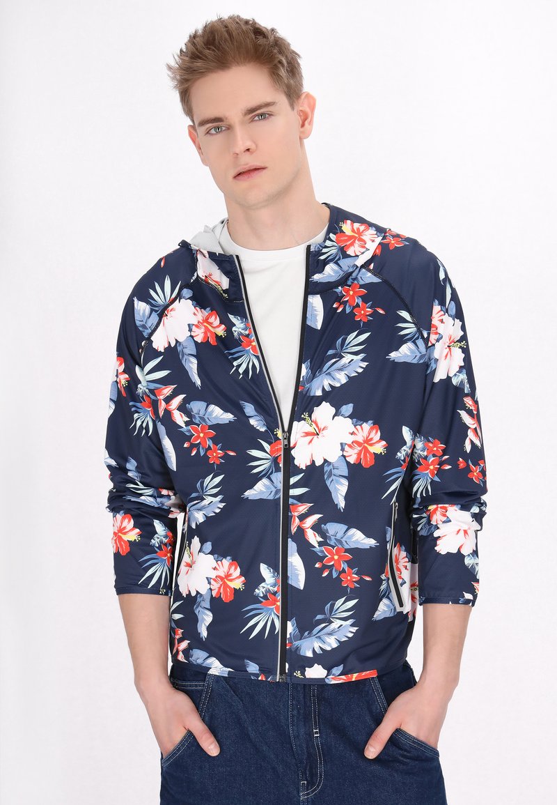 Navy bloemen-zipperjack, voorzien van rode en witte bloemen met groene bladeren. Lange mouwen met een capuchon, gestructureerde stof.
