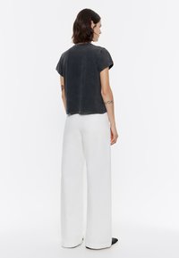 Camiseta negra de corte largo con mangas cortas enrolladas, combinada con pantalones anchos blancos. La tela tiene una textura suave y un ajuste relajado.