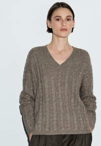 Maglione lavorato a maglia color khaki con scollo a V, caratterizzato da un motivo a treccia testurizzato, maniche lunghe e un taglio morbido. Materiale morbido e caldo.