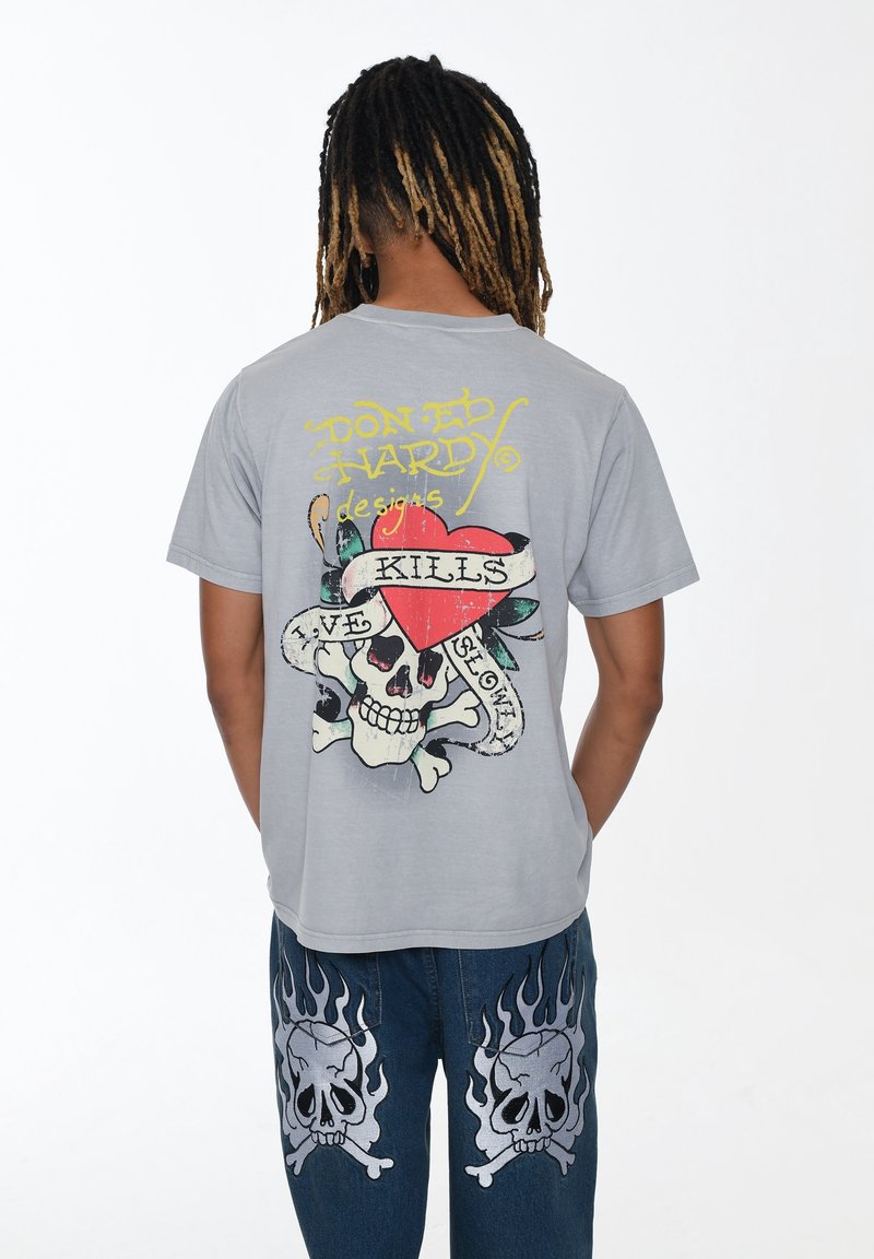 Grijze T-shirt met korte mouwen, featuring een kleurrijke schedel met een hart, baniertekst en decoratieve elementen op de achterkant.