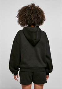 Sudadera negra de gran tamaño con capucha ajustable, puños y dobladillo acanalados. Combínala con pantalones cortos negros a juego. Textura de tela suave.