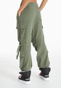 Green cargo pants with side pockets, elastic cuffs, and drawstrings. Fabric appears lightweight with a smooth texture. Worn with black sneaker boots.
