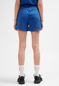 Kungablå sportshorts med elastisk midja, med en slät textur och avslappnad passform. Bärs med svarta skor och vita mönstrade strumpor.