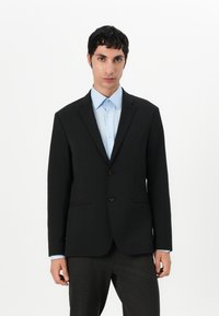 Černý šitý blazer se zapínáním na dva knoflíky, klopovým límcem a bočními kapsami, doplněný světle modrou košilí pod ním.