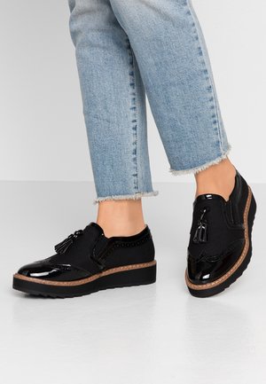 Chaussures noires à lacets avec un bout en cuir vernis, un corps en tissu texturé, des accents de franges et une semelle épaisse et striée.