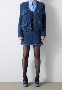 Veste en tweed bleue avec des détails en frange, jupe assortie et chemise bleu clair. Les accessoires comprennent des talons à motifs bleu et blanc.