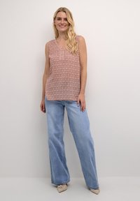 Haut sans manches rose clair avec un motif géométrique blanc, décolleté en V ; associé à un jean clair à jambes larges et des ballerines beiges.