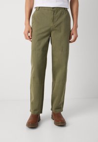 Olive green cotton pants with a straight fit, featuring reinforced knee panels and a flat front. Paired with brown leather boots.
