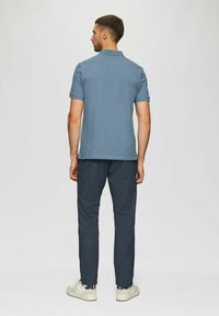 Polohemd aus leichtem Baumwollstoff in Hellblau mit kurzen Ärmeln, kombiniert mit dunkelblauen Hosen und weißen Sneakers, von hinten gesehen.