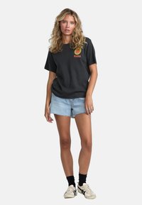 Sort kortærmet t-shirt med multicolorefprint, parret med lyseblå denimshorts. Har en afslappet pasform og en flosset kant.
