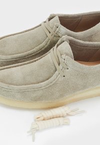 Mocassini in suede grigio chiaro con una texture morbida, dotati di lacci in cotone e suola in gomma chiara. Inclusi due paia di lacci aggiuntivi.