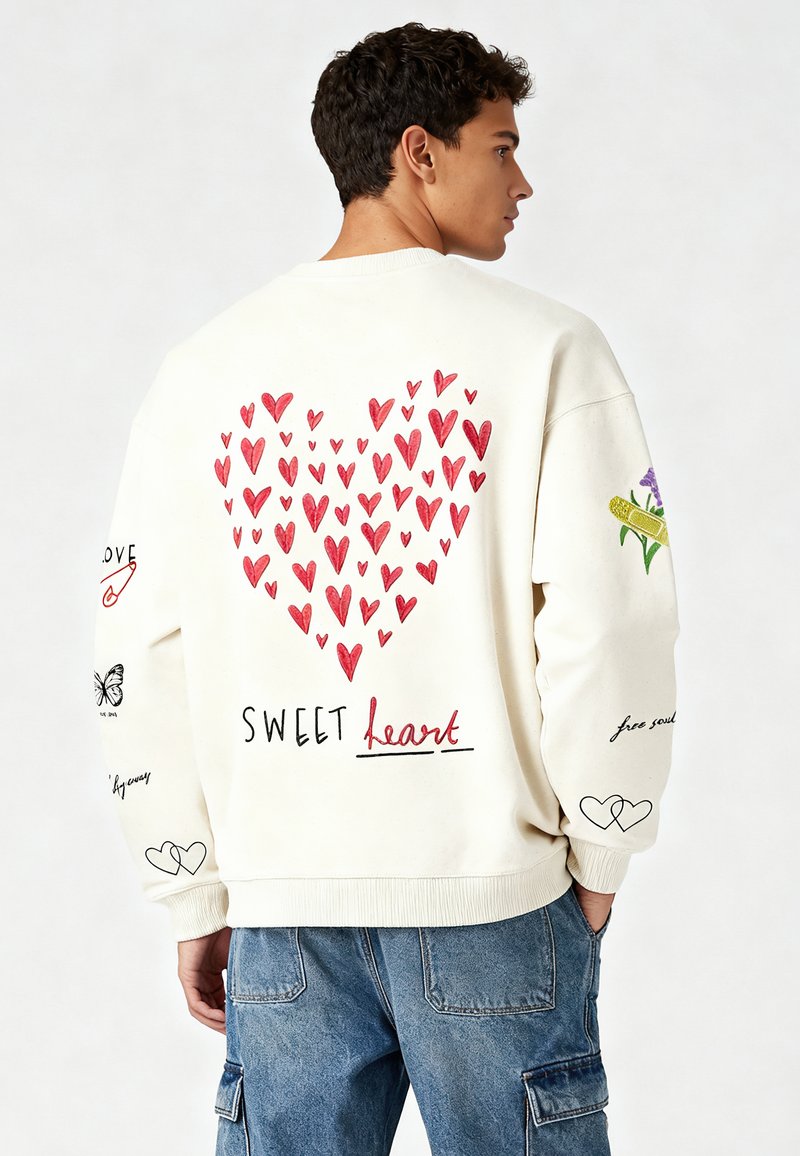 Krém színű pulóver nagy piros szívvel a hátsó részen, rajta a "SWEET heart" felirattal. A ujjakon különböző illusztrált díszítések találhatók.