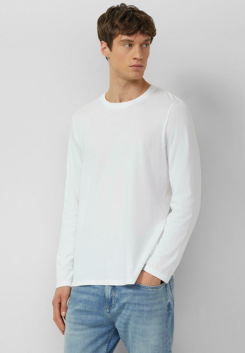 Weißes Langarmshirt mit Rundhalsausschnitt, aus Baumwolle, glatte Textur. Kombiniert mit hellblauen Jeans, die eine lässige Passform zeigen.