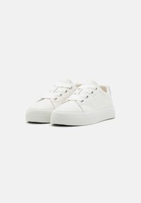 White sneakers with a smooth leather upper, round toe, flat rubber sole, and metallic accent on the heel. Features lace-up closure and stitching details.