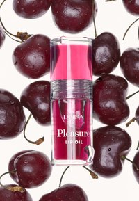 Bottiglia trasparente di olio per labbra con liquido rosa e dettagli argentati, circondata da ciliegie rosso scuro lucide, con gocce d'acqua sulla frutta.