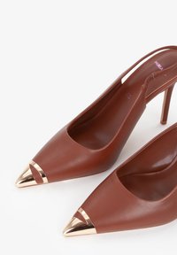 Scarpe slingback a punta in pelle marrone con tacco alto, caratterizzate da dettagli metallici dorati nella punta e un design aperto sul retro.