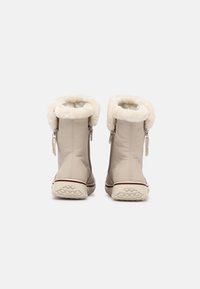 Stivali invernali beige con fodera in pelliccia visibile ai polsini, cerniera sul retro e suole in gomma testurizzata, viste da dietro su uno sfondo bianco.