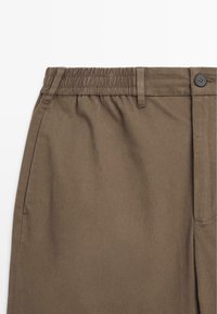Bruine katoenen broek met een elastische tailleband, featuring een knoopsluiting en zijzakken. Glad textuur met een getailleerde pasvorm.