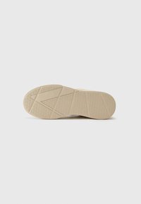Beige rubberen schoenzool met een gestructureerd oppervlak, voorzien van geometrische patronen en een gesegmenteerd ontwerp voor grip.