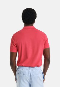 Camisa polo roja con cuello clásico y mangas cortas, hecha de un tejido suave. Combinada con pantalones cortos azul claro con una cinturilla elástica.