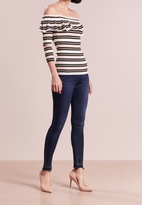 Valkoinen, musta ja keltainen, yksivärinen rypytetty off-the-shoulder -paita, yhdistettynä tummansiniset skinny-farkut ja nude-korkokengät.