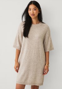 Beiges Strickkleid mit runder Halslinie und kurzen Ärmeln; lockere Passform mit geripptem Besatz an Ärmeln und Saum. Glatte Textur.