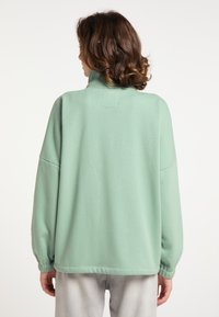 Felpa verde chiaro con colletto alto, spalle scese e polsini elasticizzati. Tessuto morbido con una texture liscia; design semplice.