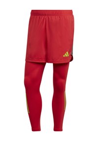 Rode sportieve shorts met een grijze accent, gecombineerd met strakke rode leggings met gele streepdetails aan de zijkanten.