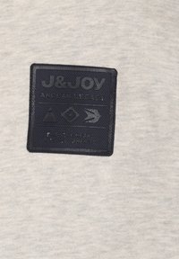 Grijze stof met een gestructureerd marineblauw label waarop de tekst "J&Joy ANDEAN LEGACY" staat, met daaronder verschillende grafische iconen.