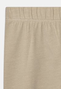 Tissu en tricot beige avec une taille élastique froncée et une texture à côtes verticales, présentant une surface lisse et un aspect doux.