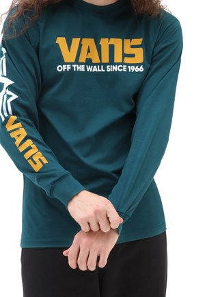 Camiseta de manga larga color verde azulado hecha de algodón, con texto gráfico "VANS" en amarillo y blanco en el frente y a lo largo de las mangas. Textura suave.