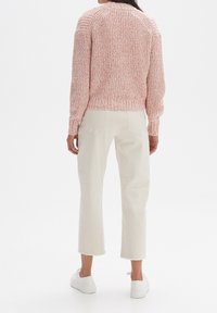 Texturovaný růžový svetr s kulatým výstřihem a ribbovaným lemem, kombinovaný s béžovými zkrácenými kalhotami a bílými teniskami.