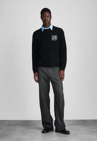 Black sweater with a wolf motif, paired with a light blue collared shirt and gray trousers. The outfit is completed with black shoes.