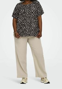 Top s krátkým rukávem s leopardím potiskem v kombinaci s krémovými volnými kalhotami a béžovými teniskami. Volný střih, měkká tkanina a jemný lesk na texturách.