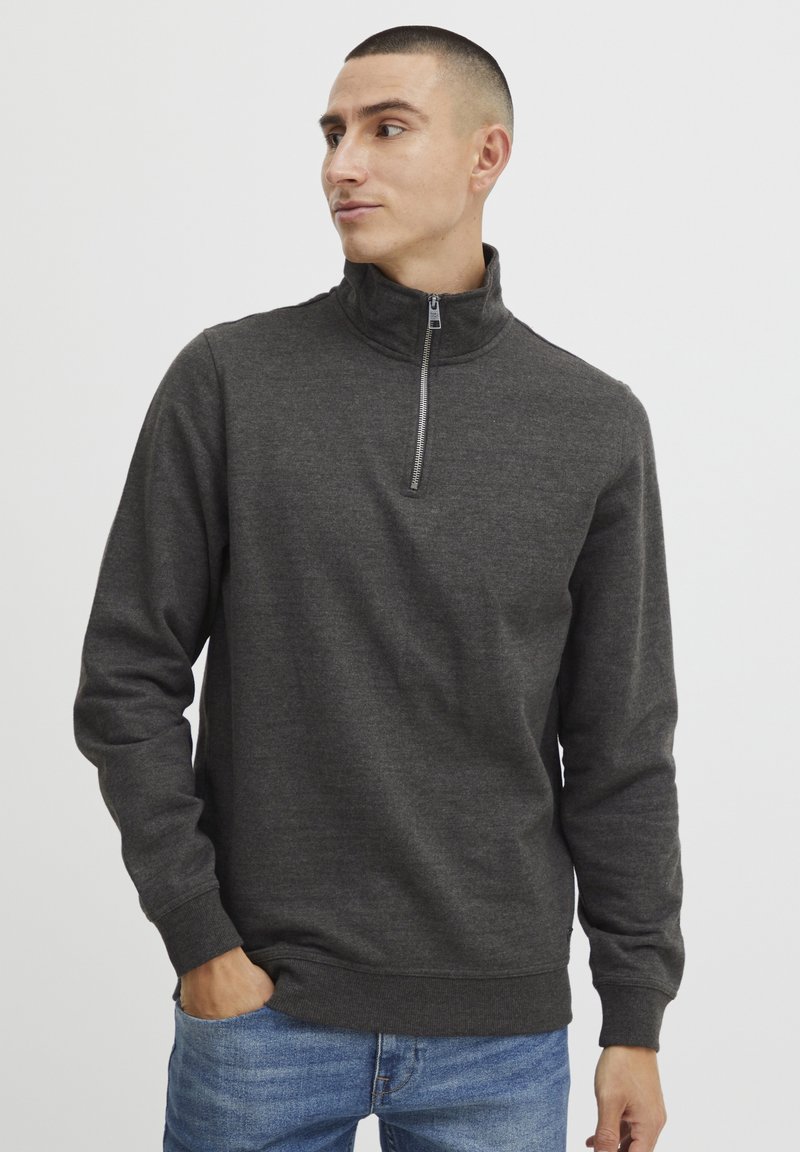Felpa grigio scuro con zip e collo alto, maniche lunghe, texture morbida, polsini e orlo a coste, abbinata a jeans blu. Design semplice e minimalista.