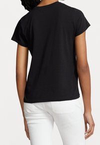 T-shirt noir à manches courtes en tissu doux, avec un col rond et une coupe décontractée. L'ourlet est droit sans logos ni embellissements visibles.
