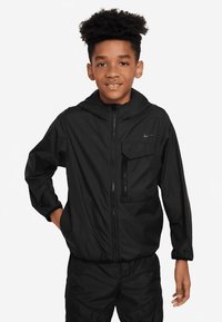 Μαύρο ελαφρύ μπουφάν με κουκούλα, φερμουάρ μπροστά και θήκη στο στήθος. Φτιαγμένο από απαλό ύφασμα με μικρό λογότυπο στην αριστερή πλευρά.