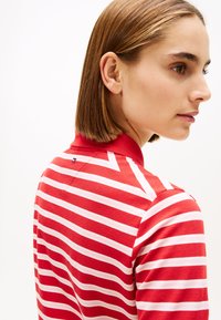 Punase ja valge triibuline polosärk kraega, millel on väike logo kaela tagaosas lähedal. Pehme kangas ja istuv disain.