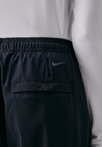 Černé sportovní šortky s elastickým pasem, zapínací zadní kapsou a malým šedým logem Nike na boku. Hladká, lehká tkanina.
