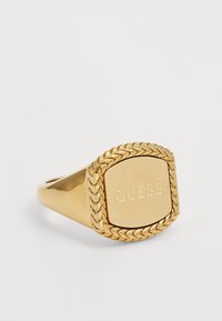 Gullring med firkantet topp hvor "GUESS" er gravert, omgitt av en fletteaktig tekstur. Glatt band med polert finish.