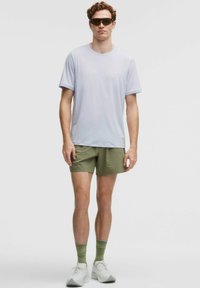 Licht paarse T-shirt met korte mouwen, olijfgroene shorts, groene geribbelde sokken, zonnebril en witte sportschoenen. Eenvoudig ontwerp, lichtgewicht stof.