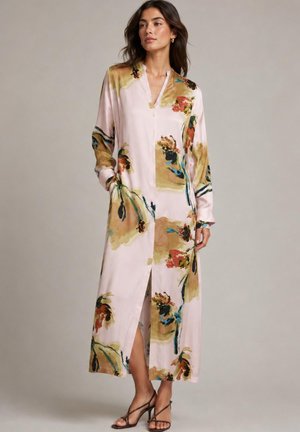 Kvinde iført en lang, lyserød kjole med abstrakte blomsterprint i brun, orange, blå og grøn, kombineret med sorte, strop-sandaler.